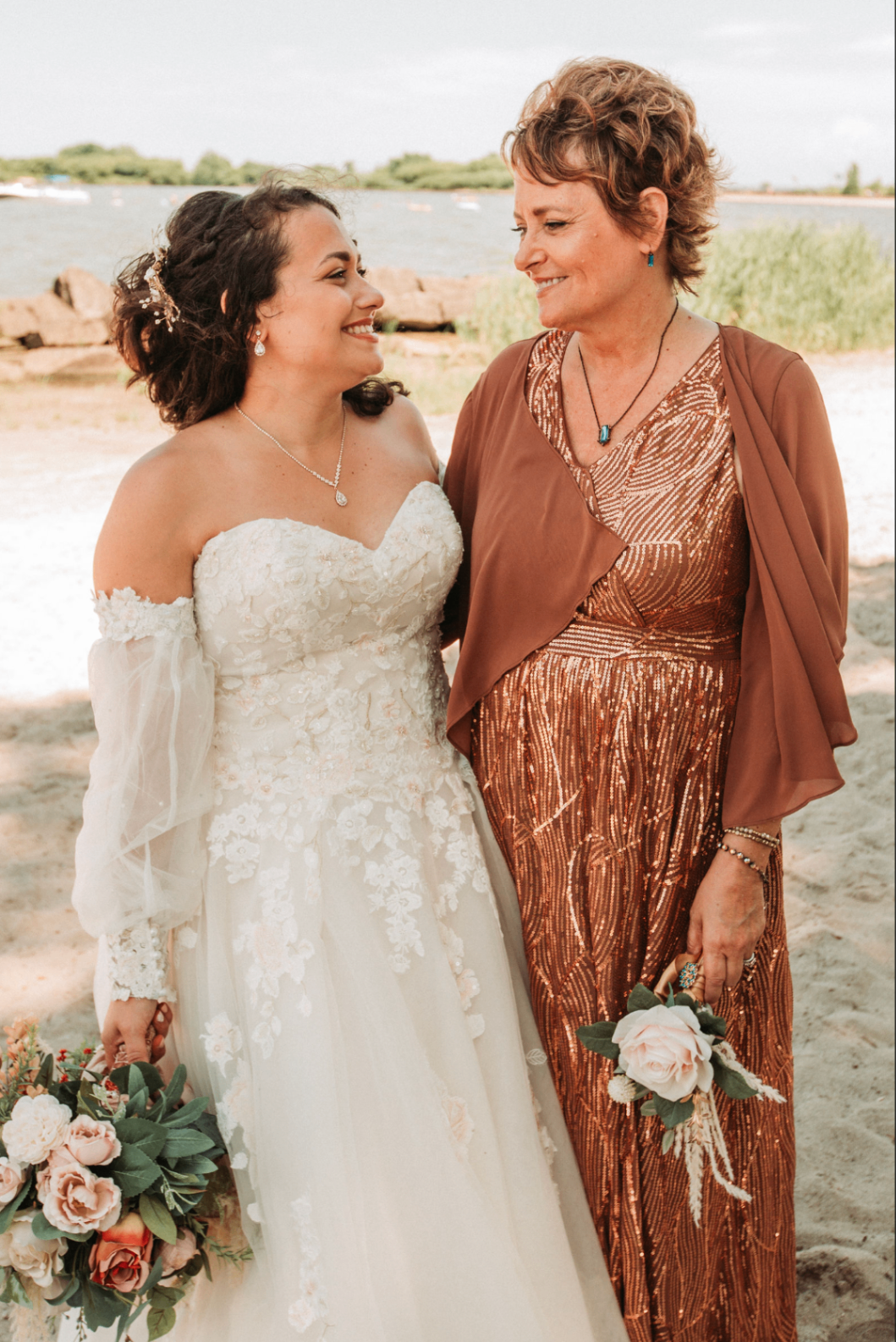 Jessie smiling at an older woman in a copper sequin dress while holding her bouquet on the beach