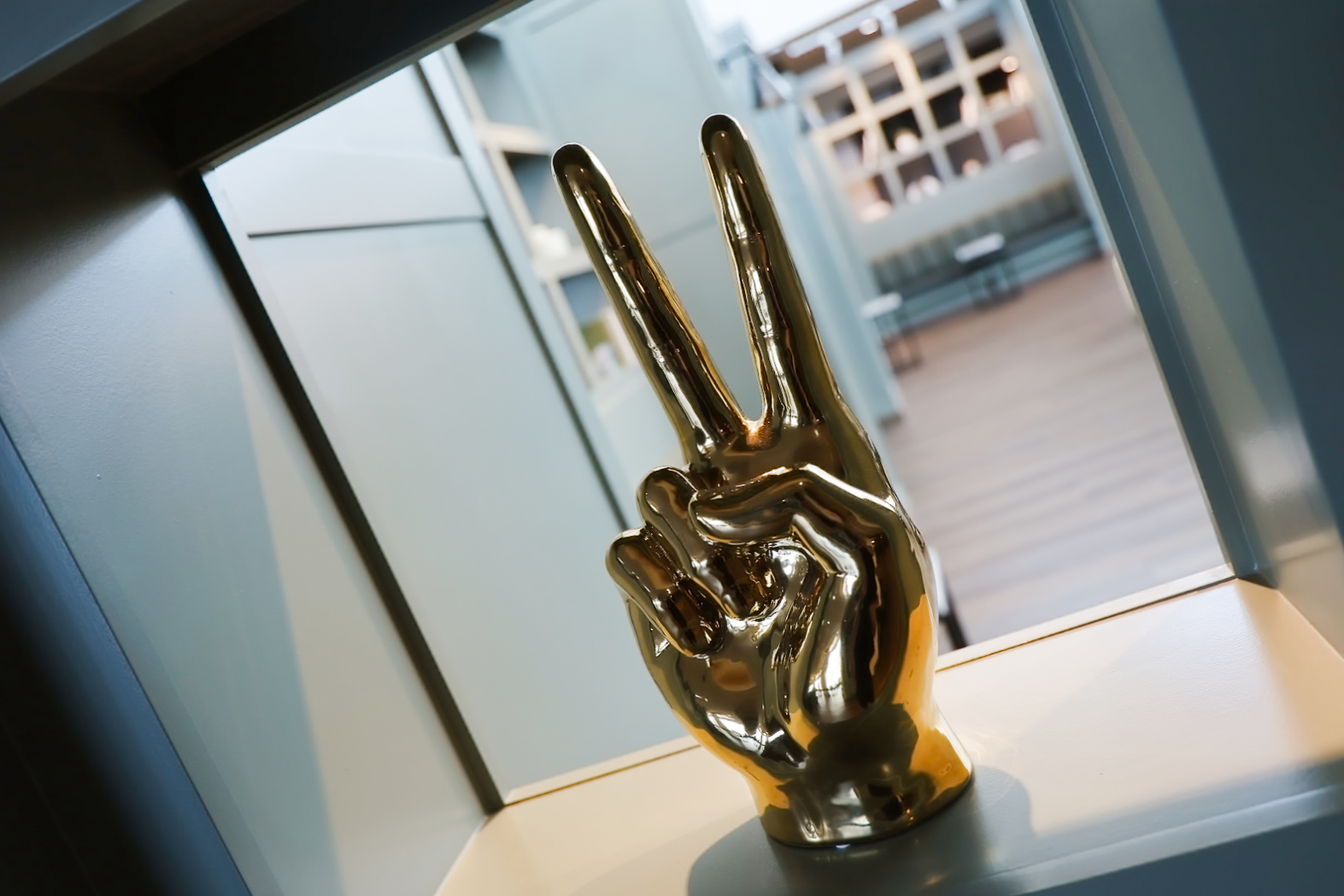 Polished brass peace-sign sculpture on a windowsill