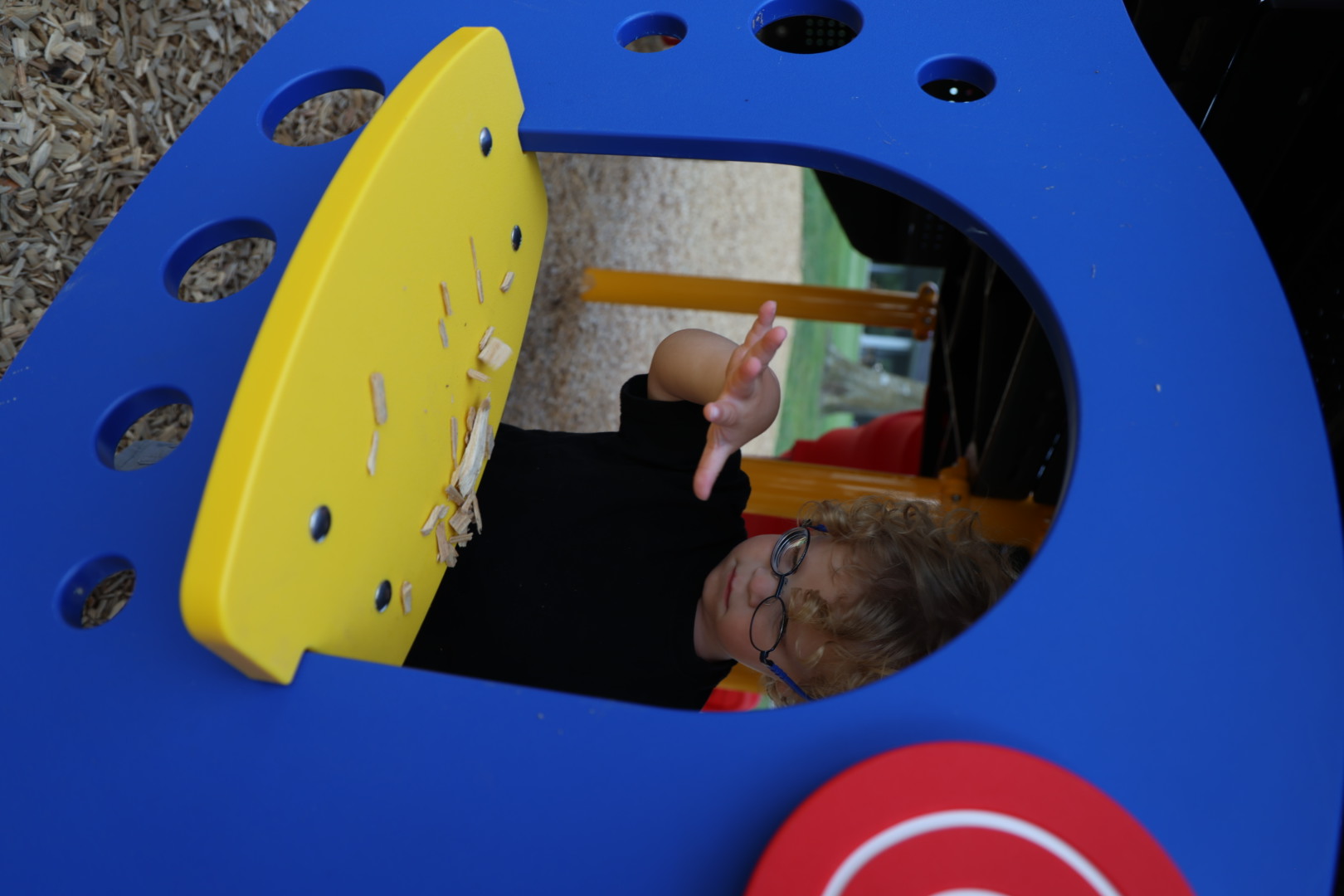 Boy tossing woodchips off the yellow window ledge of the play structure