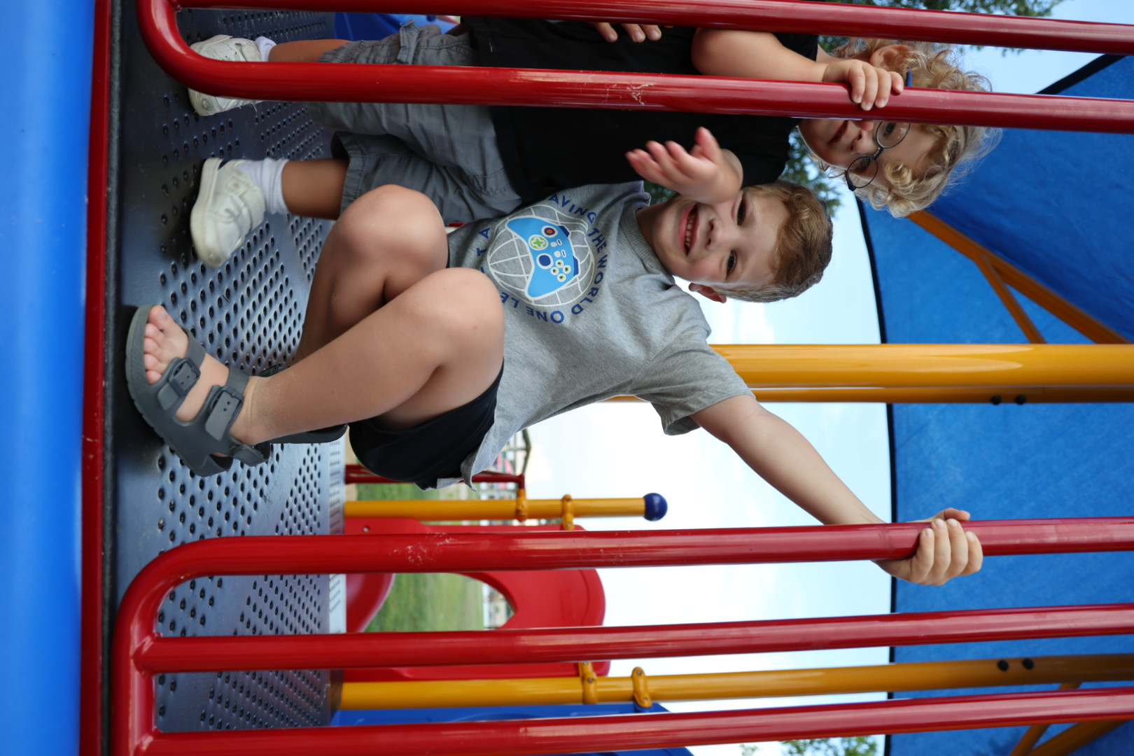 Two brothers together on the play deck, one crouched grinning, the other peeking through the bars