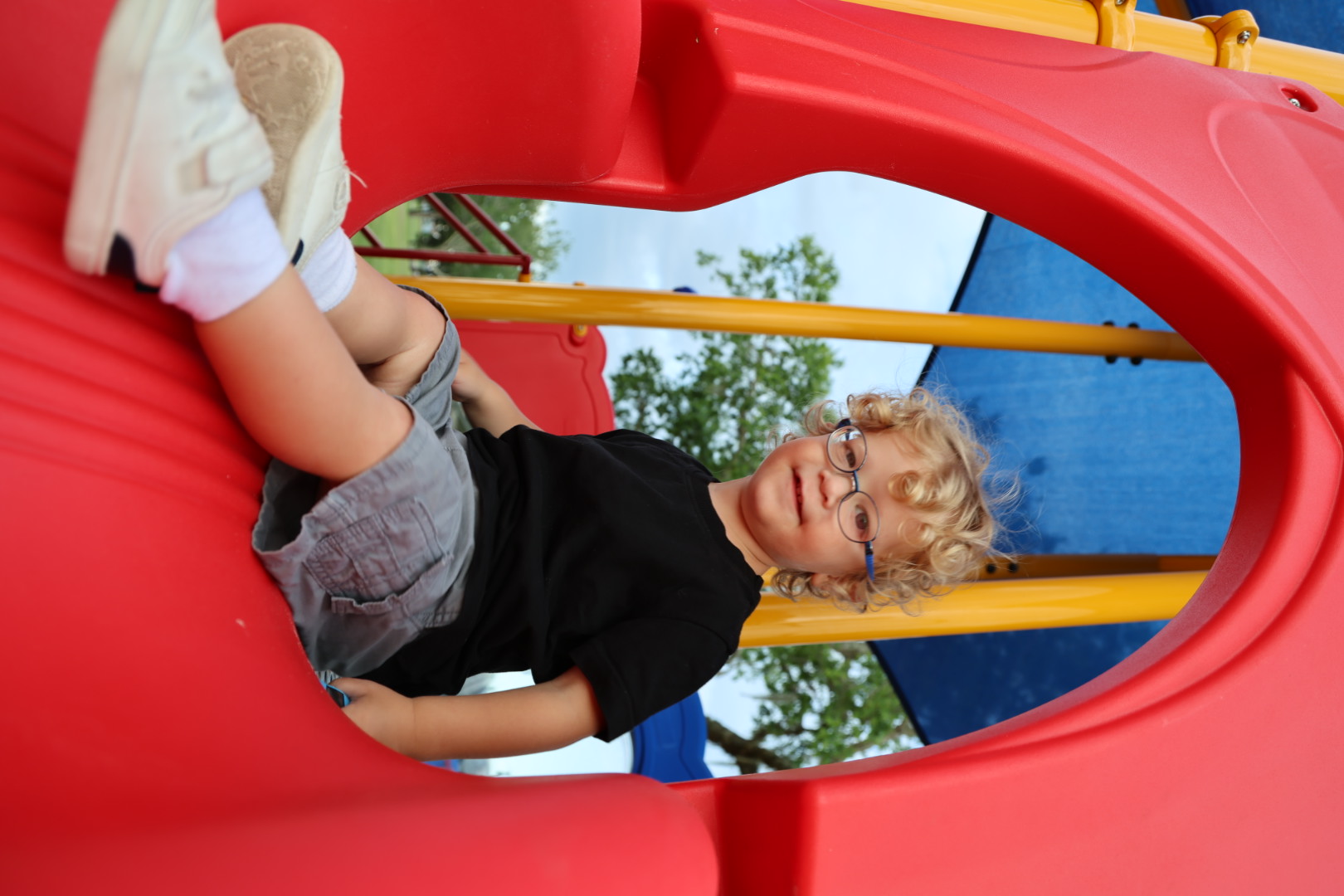 Boy in a black shirt sitting inside a red slide tunnel