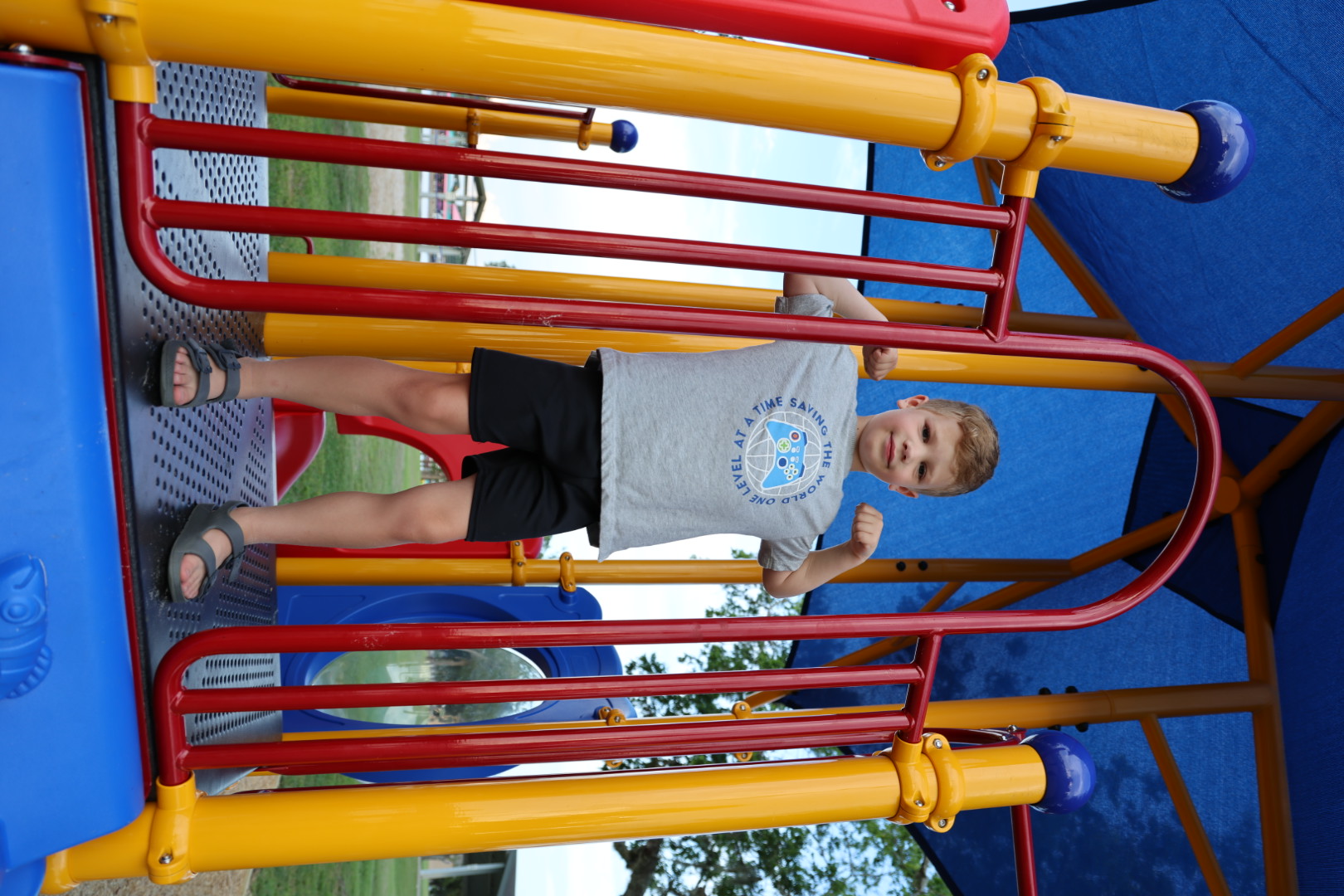 Boy in a gray tee flexing his arms on the top deck of the play tower