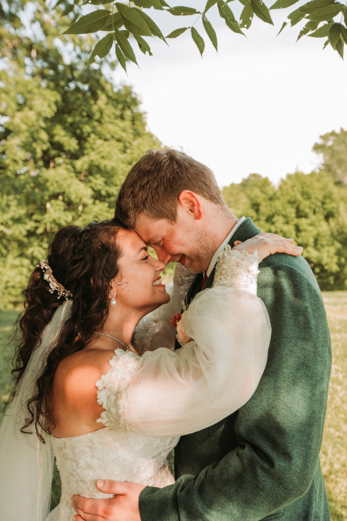 Jessie and Kurtis forehead to forehead under the trees, arms around each other