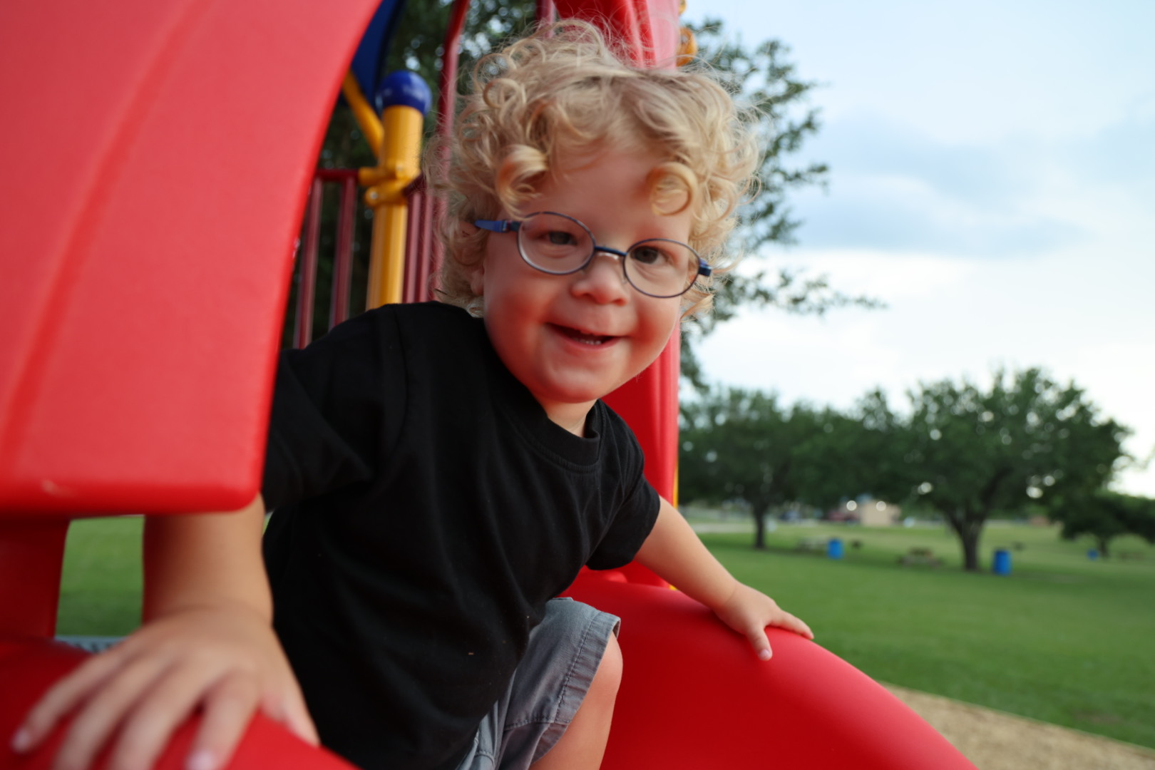 Curly-haired boy grinning while climbing on a red play structure at the park