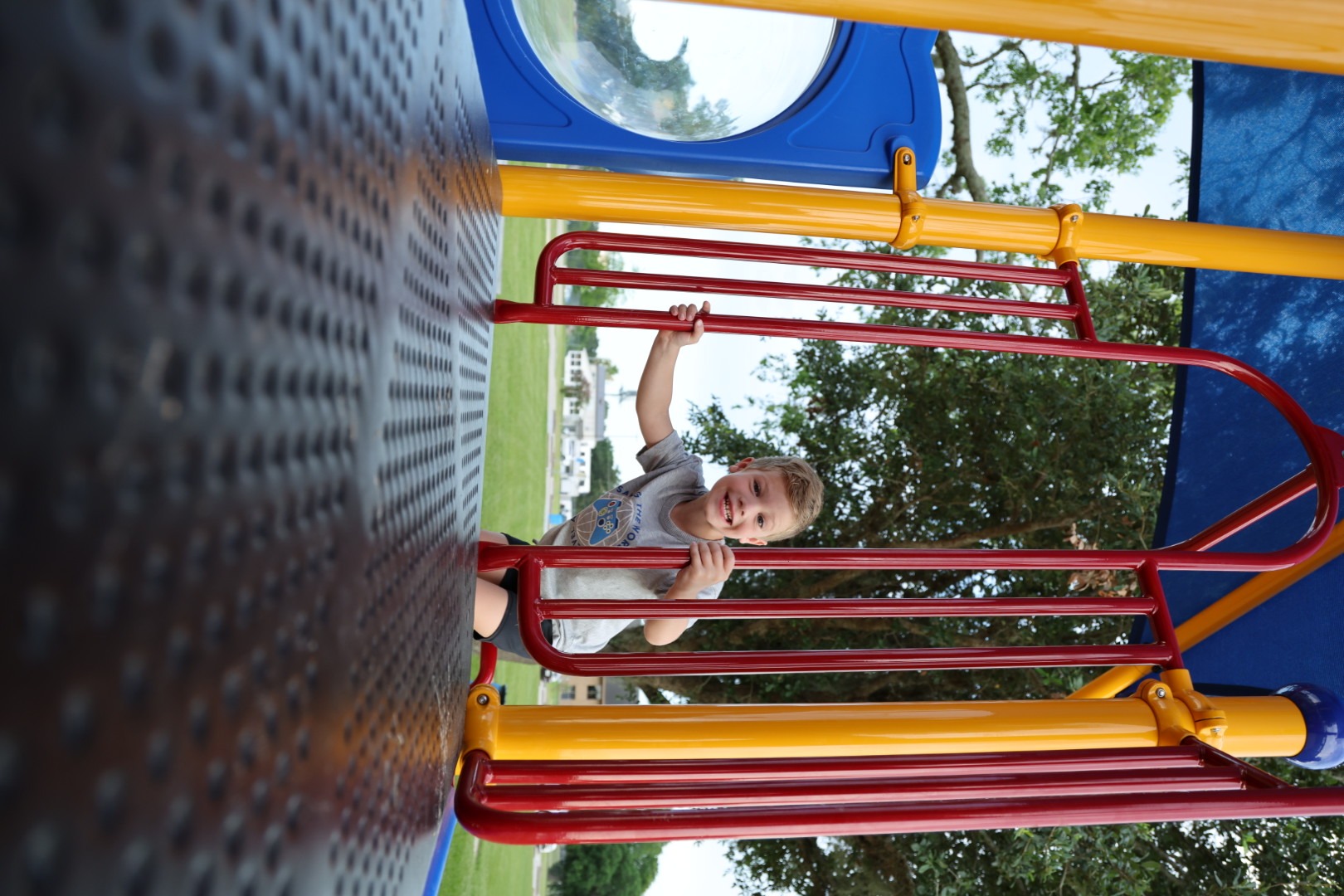 Boy grinning through the red bars at the top of the play tower