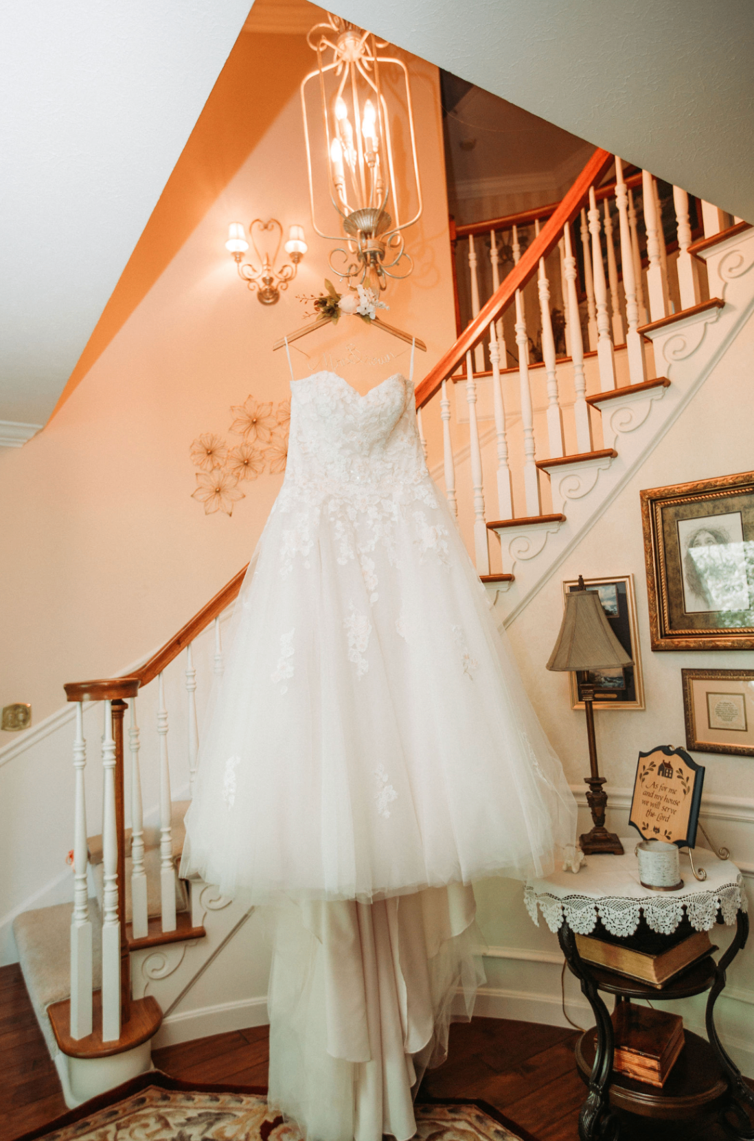 Bridal gown hanging from a chandelier on a curved wooden staircase