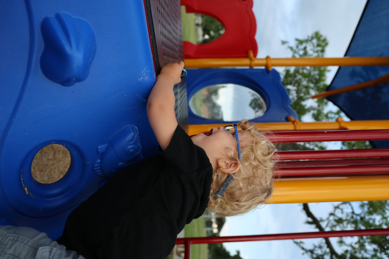 Boy laughing on the play structure, mouth wide open, colorful bars around him