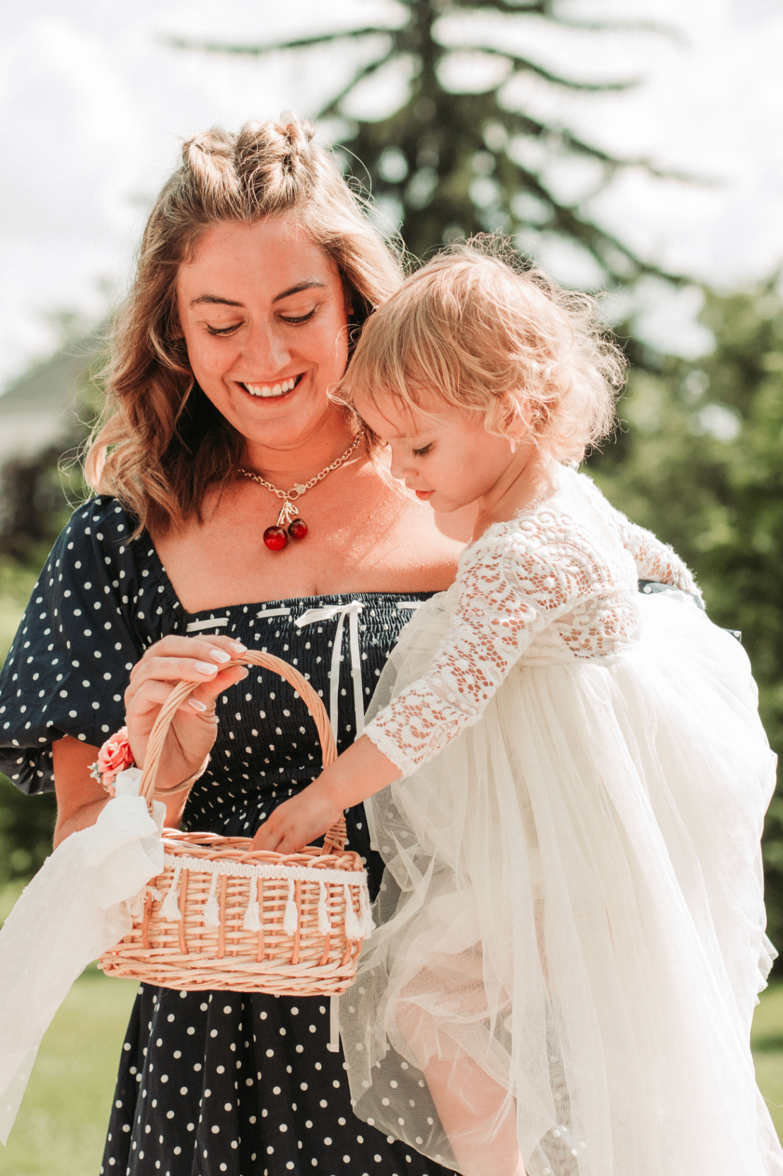 Woman in polka dot dress smiling with a toddler flower girl holding a basket