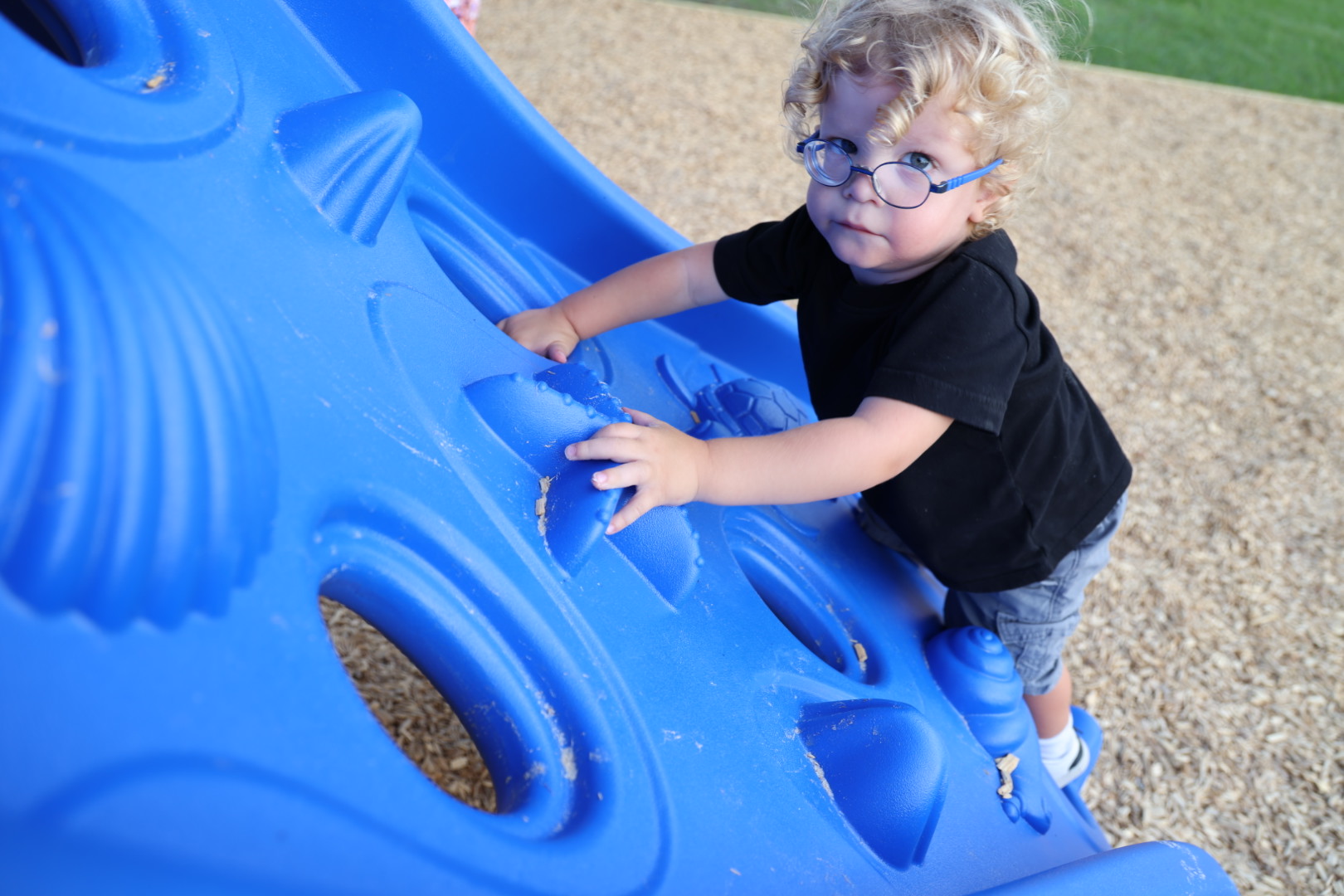 Curly-haired boy in blue glasses climbing up the blue textured wall
