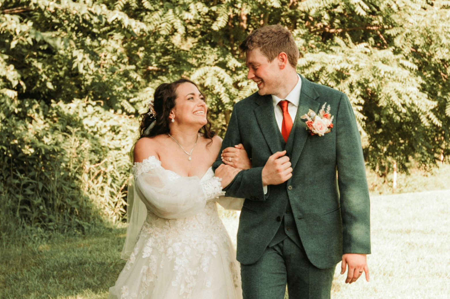 Jessie laughing on Kurtis's arm as they walk through the sunlit grass