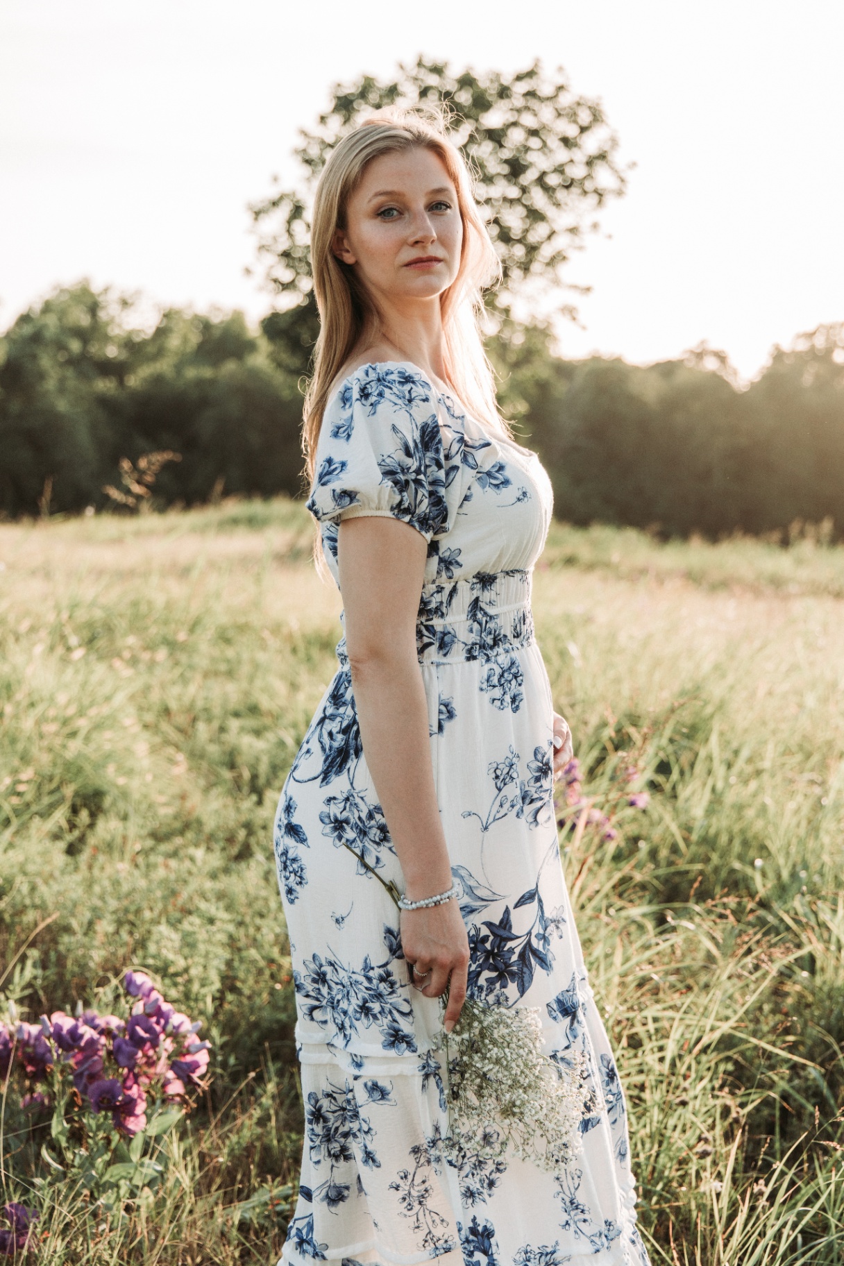 Naomi standing in a meadow at sunset, wildflowers in hand