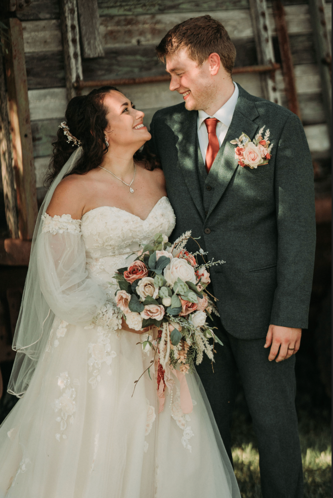 Jessie and Kurtis smiling at each other, bouquet between them