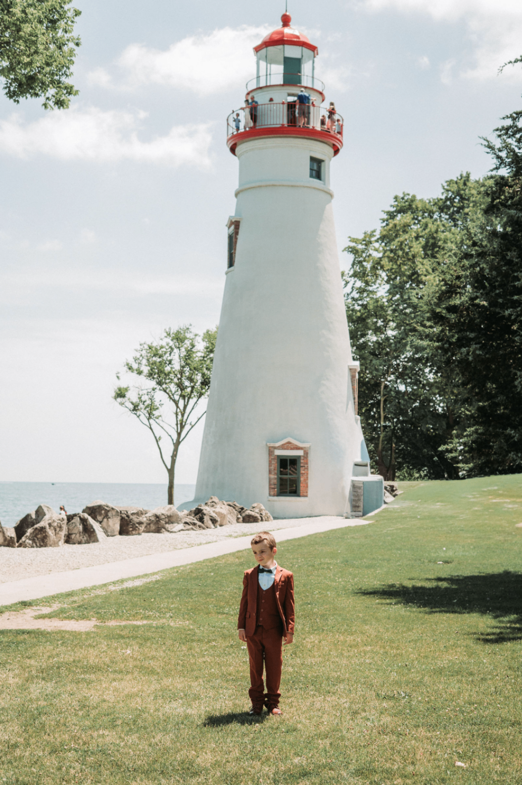 Young boy in a rust-colored suit standing in front of the Marblehead lighthouse