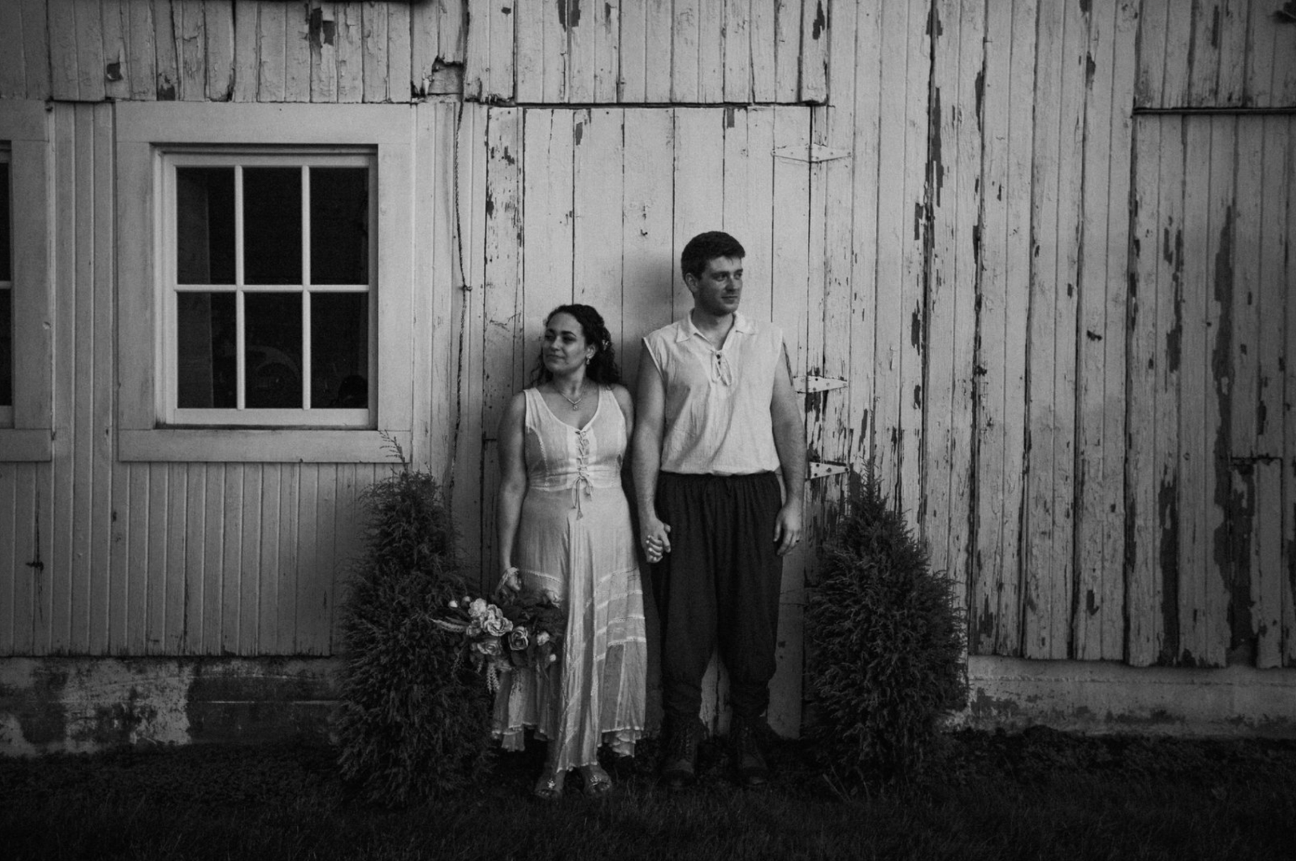 Black and white portrait of Jessie and Kurtis holding hands in front of the barn doors