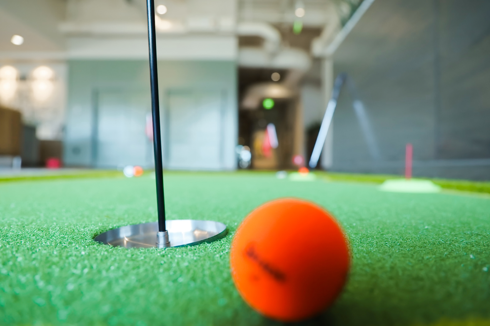 Orange golf ball beside the cup on an office putting green