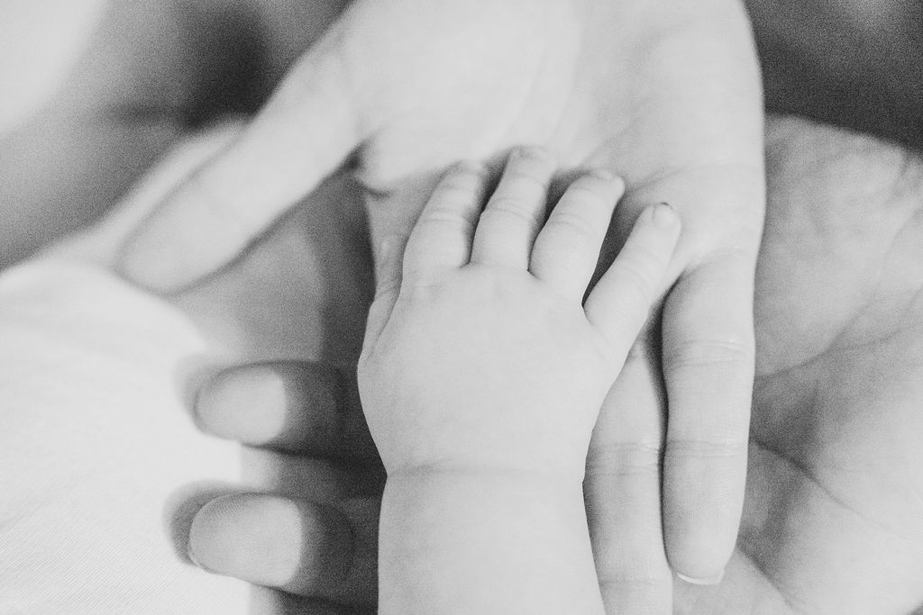 Black and white photograph of a baby's hand resting in a parent's hand